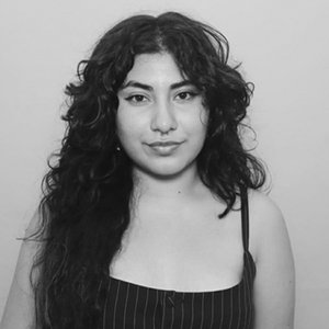 A black-and-white headshot of a woman with dark curly hair against a white background.