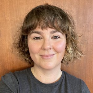 A portrait headshot of a poet with a bob haircut against a wooden background.