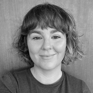 A portrait headshot of a poet with a bob haircut against a wooden background.