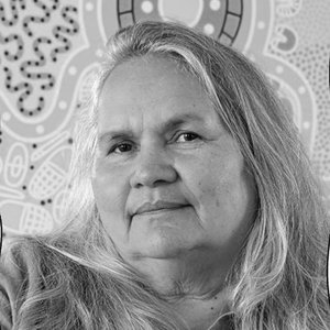 A black and white portrait image of a woman against a background of Aboriginal art.