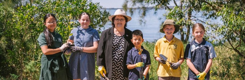 The winners of Poem Forest 2025 standing outdoors in a line with certificates and native tree seedlings.