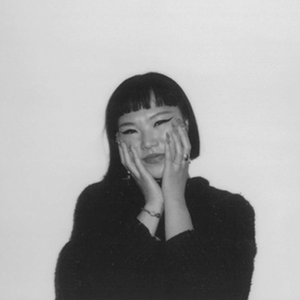 A polaroid photo of a woman in a black shirt, hands on her cheeks, looking into the camera.