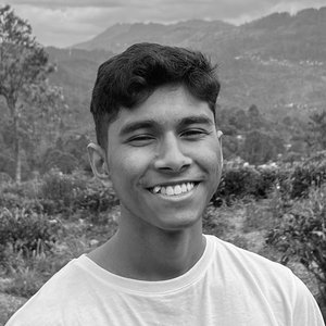 Black-and-white portrait headshot of a smiling man in a white shirt against a background of lush grasses, trees, and mountains.