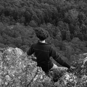 A black-and-white shot of the poet sitting on rocks, looking out over mountains and bushland.