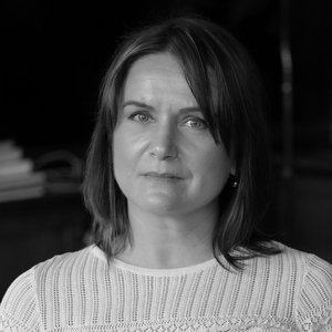 A portrait headshot of a woman with straight, brown hair and a white crochet top.