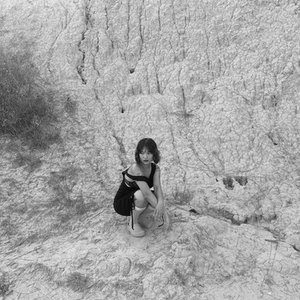 A black and white headshot of a woman crouching on dry terrain.