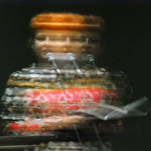 A blurry, stylised portrait of a poet with bright orange hair reading from a book.