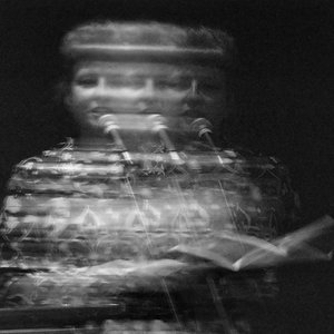 A blurry, stylised portrait of a poet standing at a microphone and reading from a book.