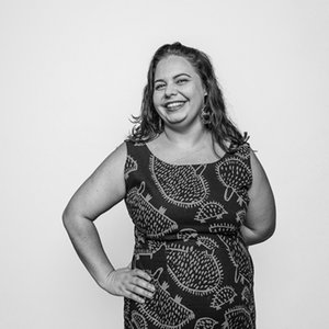 A black-and-white shot of a woman in a dress with her hand on her hip against a white background.