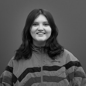 A black-and-white headshot of a woman with dark hair, smiling and wearing a striped jumper.