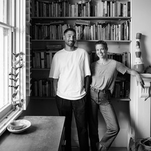 A black-and-white shot of two people standing together in a well-lit room in front of a bookshelf.