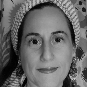 A portrait shot of a woman with striped headwear, gold earrings, and a colourful floral background.